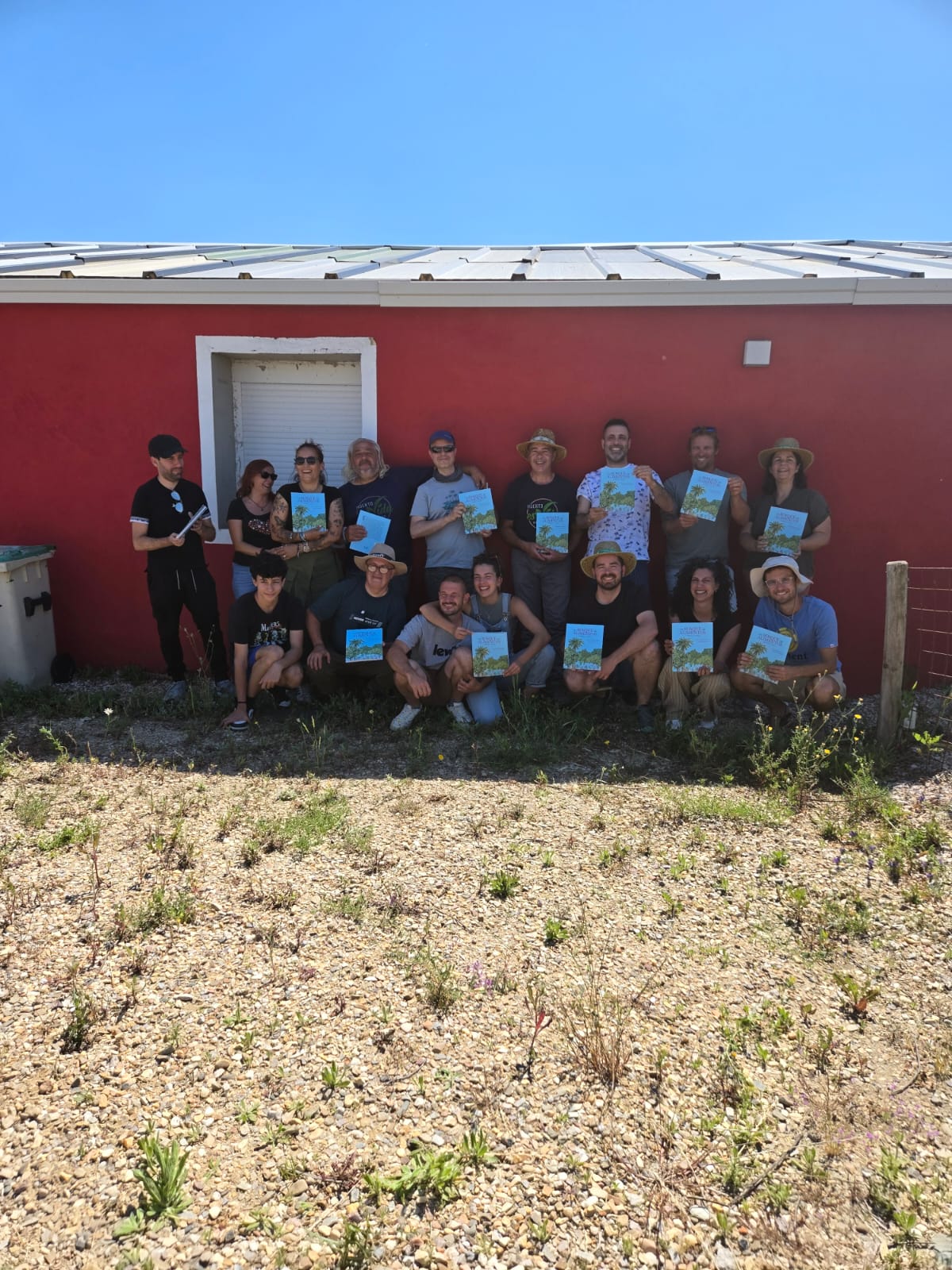 Grupo de participantes posando con el libro «Un bosque de alimentos» frente a una casa roja en Moderny Farmily.