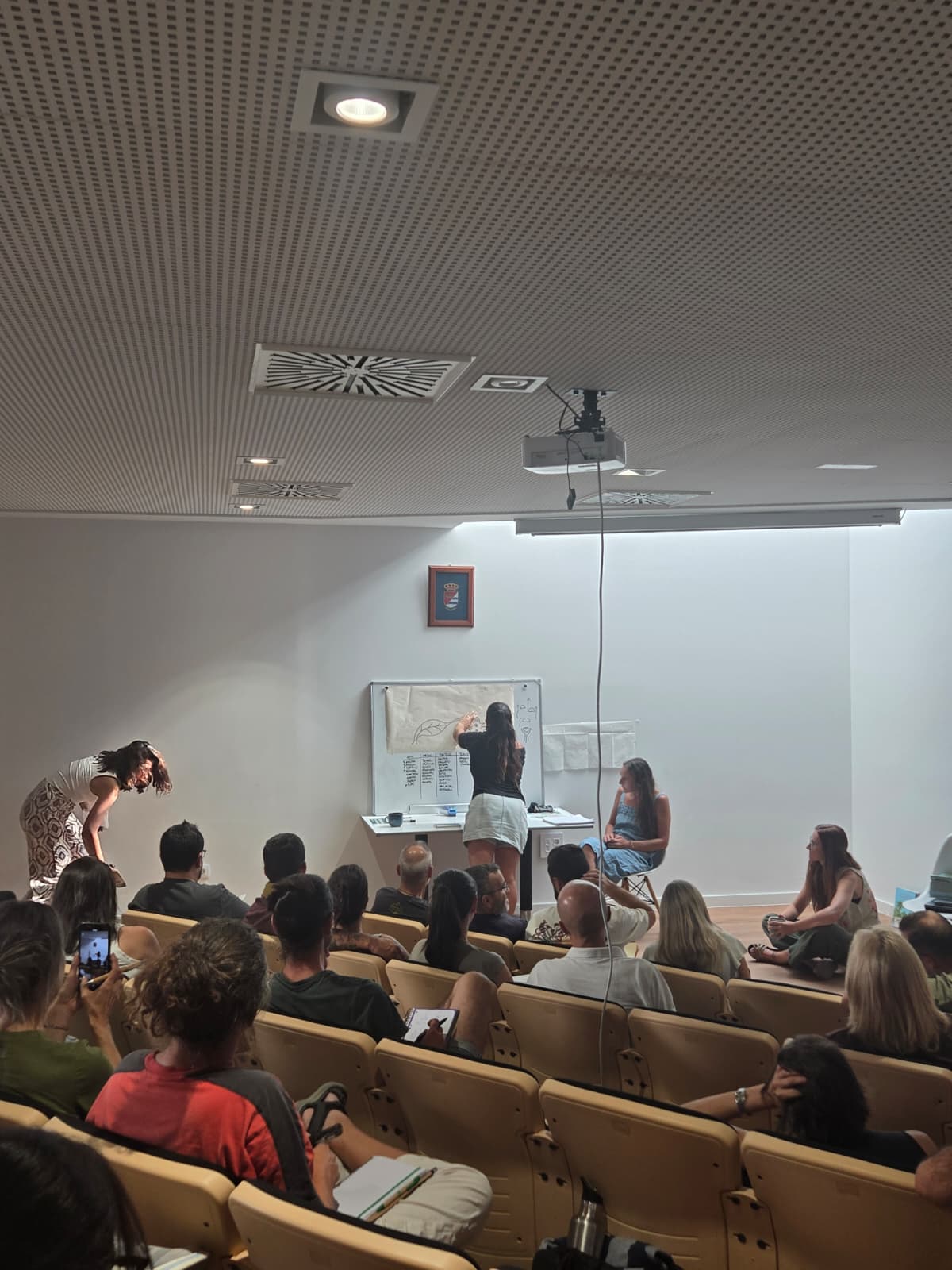 Formadoras explicando el diseño de un bosque de alimentos en pizarra ante el grupo, durante el taller en Villalbilla.